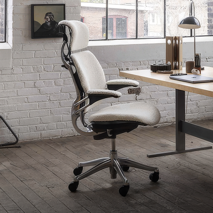 Spacious loft office with large windows, white brick walls, and hardwood floors. A modern desk and ergonomic chair create a bright, airy workspace.