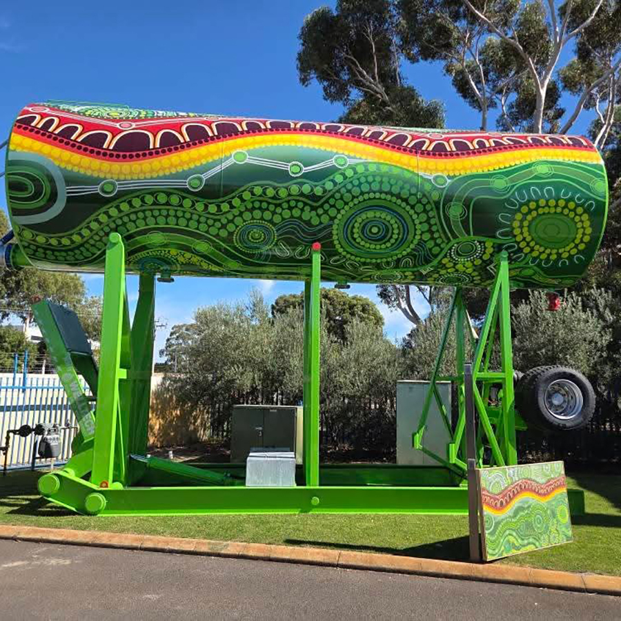 A large, vibrantly painted can sculpture with indigenous-style patterns stands on a bright green frame