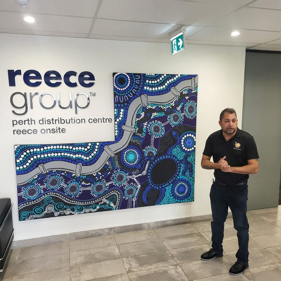 Kevin Bynder stands next to a colourful Aboriginal artwork featuring circular patterns in blues and purples