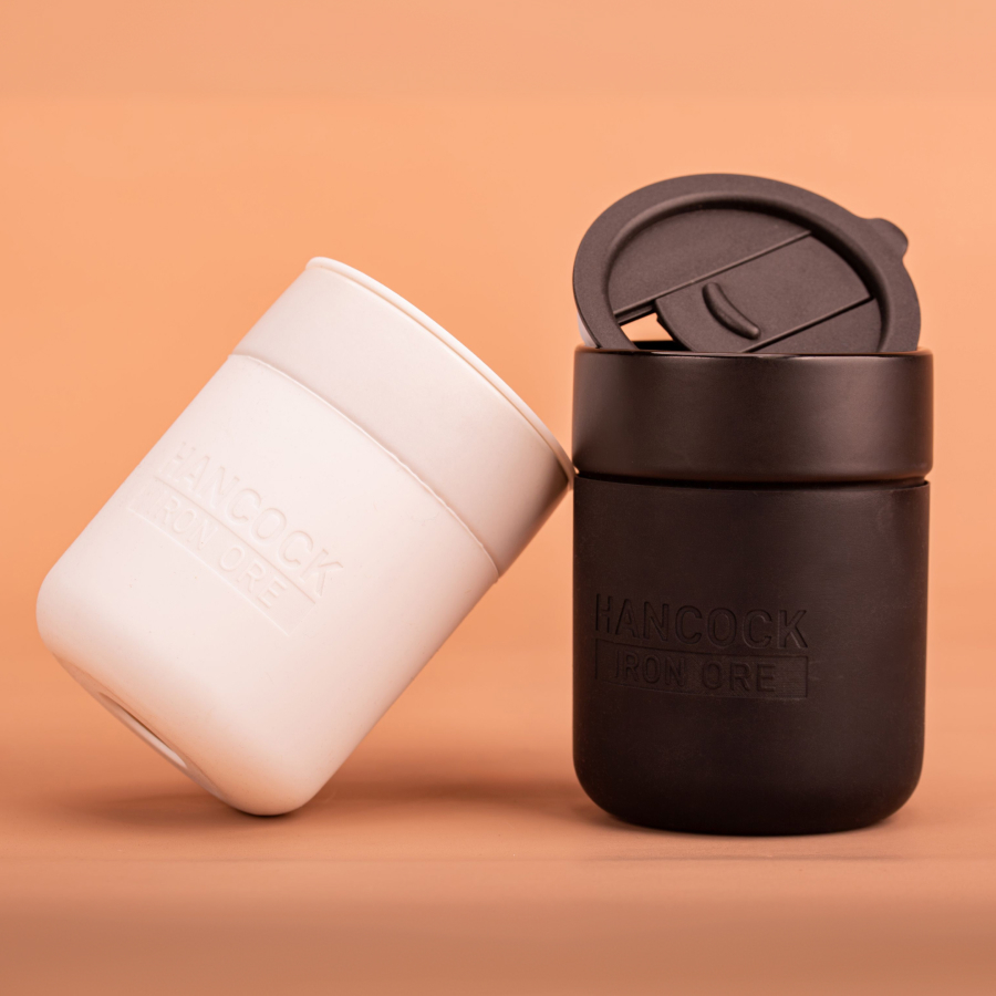 Two reusable cups, one white and one black, are placed against a peach background.