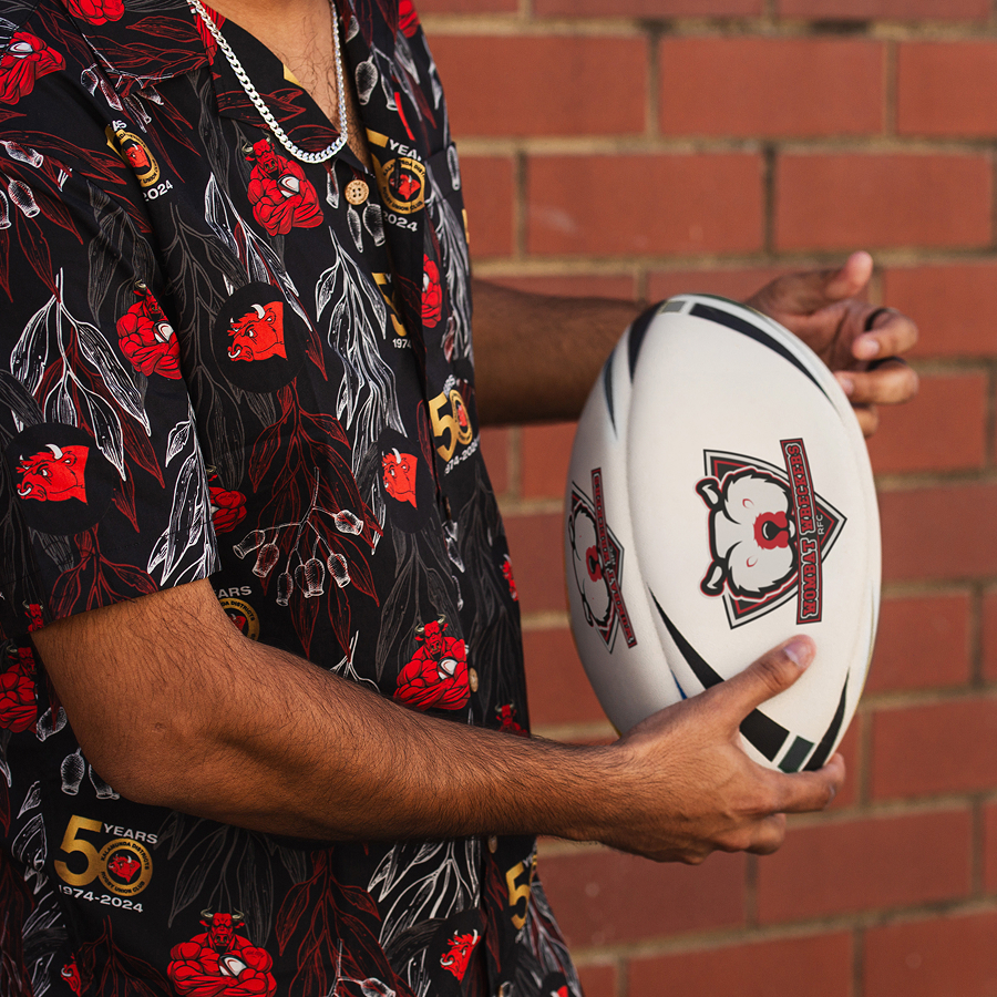 A person in a floral and logo-patterned shirt holds a rugby ball with a team emblem.