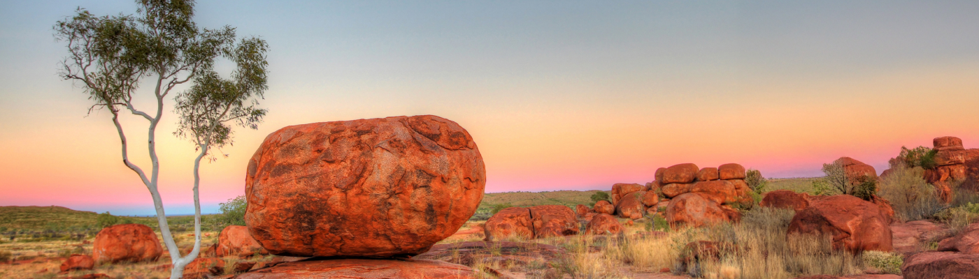 A serene landscape at sunset, featuring large red rock formations and a single, slender tree