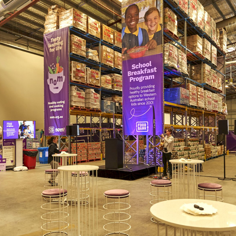Warehouse event for a School Breakfast Program, featuring stacked food pallets, tables, and vibrant banners promoting healthy meals for students.