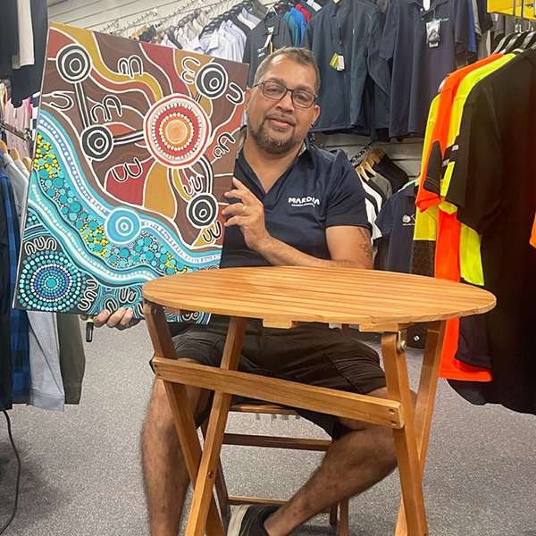 Kevin Bynder holding up a vibrant Indigenous art with earth tones and blue patterns