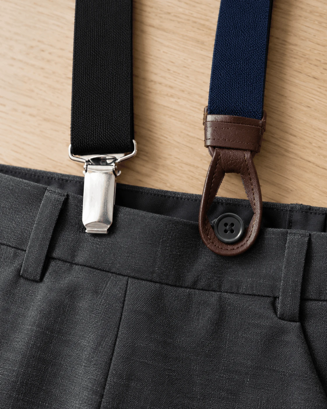 Close-up comparison of a clip-on suspender attachment and a button-on leather suspender ear on a pants waistband