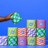 Hand holding a Who Gives A Crap toilet paper roll in front of stacked colourful rolls on bright blue background