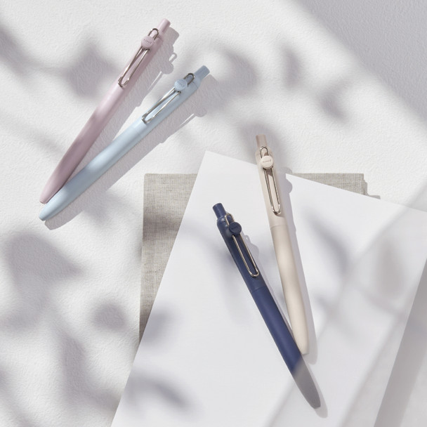 Uni-ball Zento pens in lavender, cloud blue, ivory, and indigo barrels arranged on white surface with shadows