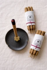 Cosmic Provisions hand rolled Palo Santo incense bundles beside a lit incense stick in a ceramic holder.
