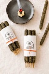 Cosmic Provisions hand rolled Palo Santo and Myrrh incense bundles with one incense stick burning in a ceramic holder.