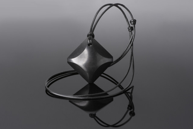 A polished black shungite pendant in a Four Elements shape on an adjustable black cord, lying on a light surface.