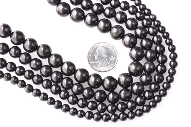 Shungite Type II beads in 6, 8, 9, and 10mm sizes compared to a US quarter coin for scale, showing polished black finish and consistent round shape.
