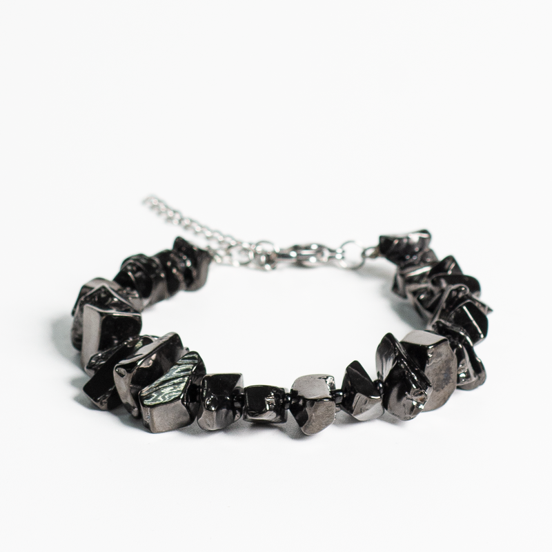 Elite Type I Shungite bracelet with silver metallic luster, laying flat on a white marble surface. Close-up shows polished stone texture.