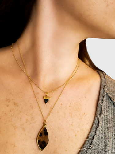 Woman Wearing Layering Necklaces Including Gold Beaded Necklace Accentuated With Dainty Aya Gold And Black Geometric Triangle Stone Pendant And Sloane Necklace Accentuated With Andrea Diamond Leopard Textured Charm | Mojo Supply Co