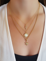 Woman Wearing White Shirt and Three Gold Necklaces. Top Necklace is Dainty Gold Necklace Chain with Rounded Dainty Ankh CZ Stone Cross Pendant, Middle Necklace is Beaded Gold Chain with Round White Shell and Gold Ball Detail Pendant, Bottom Necklace is Emily Gold Link Chain with Mary Jane CZ Pave Leaf | Mojo Supply Co