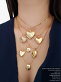 Woman Wearing 7 Gold Filled Necklaces Layered With A Gold Heart Engraved Pendant, A Gold Shell Charm, Plain Heart Charm, Heart CZ Pendant, Gold Round Moon Charm And An Oval Gold Breast Cancer Awareness Locket Pendant | Mojo Supply Co