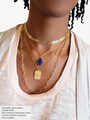 Woman Wearing A White Shirt And 4 Gold Chain Necklaces. An Arrow Choker Necklace, A Gold Necklace Layered With Blue Crystal Charm, Another Gold Chain Layered With Gold Raised Evil Eye Pendant And A Long Length Paperclip Chain Necklace | Mojo Supply Co