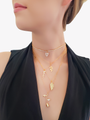 Woman In Black Dress Wearing Layered Gold Necklaces Including Gold CZ Tiny Leaf Pendant, Three Different Types of Gold Branch Charms and Gold Rose Pendant