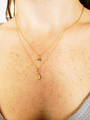 Woman Wearing Dainty Layered Gold Necklaces With a Green Tiny Leaf Charm and Round Star Charm