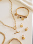 Collection of Elegant Gold Jewelry Laying in Display. 1 Gold Round Paperclip Toggle Necklace Chain.  1 Gold Arrow Custom Necklace Chain. 1 Gold Bead Ball Bracelet. 3 Small Gold Plated Stainless Steel Padlock Charms. 1 Gold Stainless Steel Hope Bracelet Bar with 3 Bracelet Charms; 1 Cubic Zirconia Initial Letter Charm, 1 Dainty Black and Gold Marble Arrow Charm, 1 Gold Stainless Steel Padlock Charm