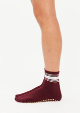 THE UPSIDE women’s maroon Adesa Grip Sock has a midi ankle fit with lemon grip on the sole and cream, yellow, and blue stripes at the ankle. Made for yoga and pilates.