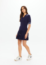 THE UPSIDE women's navy tennis Plume Knit Collared Dress fits true-to-size and features a drop waist with gathered skirt and a drawcord with tennis charms.