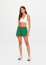 THE UPSIDE women's green recycled Austen Run Short made from quick drying performance fabric features a curved hem with cotton lace scalloped edge detailing, navy in-built shorts and invisible zip pockets. Made for running, tennis, golf & pickleball.