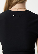 THE UPSIDE women's black Divina Isabella Baby Tee is designed for a soft and supportive fit in cotton modal fabrication and features a printed logo arrow in cream. Made for lifestyle.