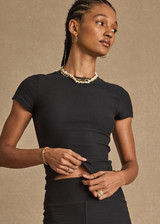 THE UPSIDE women's black Divina Isabella Baby Tee is designed for a soft and supportive fit in cotton modal fabrication and features a printed logo arrow in cream. Made for lifestyle.