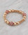 A pavé crystal bracelet with pink sparkles and gold beads displayed on a marble surface. View Product Image