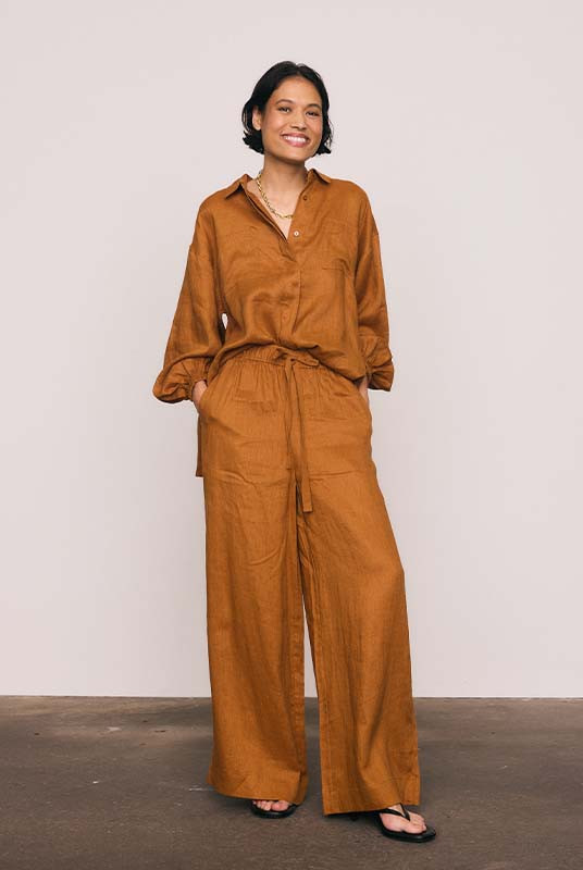 These rust linen wide-leg pants combine effortless comfort with elevated tailoring. The elasticated waist with drawcord and side pockets create a laid-back yet polished silhouette, perfect for both sunlit mornings and twilight dinners. Wear with the Rust Billow Shirt for easy, relaxed style.