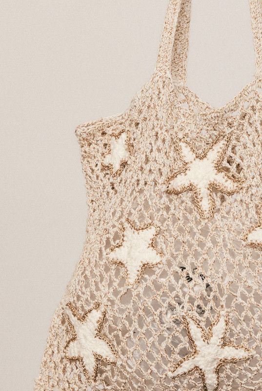 Hand-crocheted from cream cotton with a touch of gold lurex, this small tote features an intricate shell motif and soft structure—an artful accent for sunlit, effortless days.