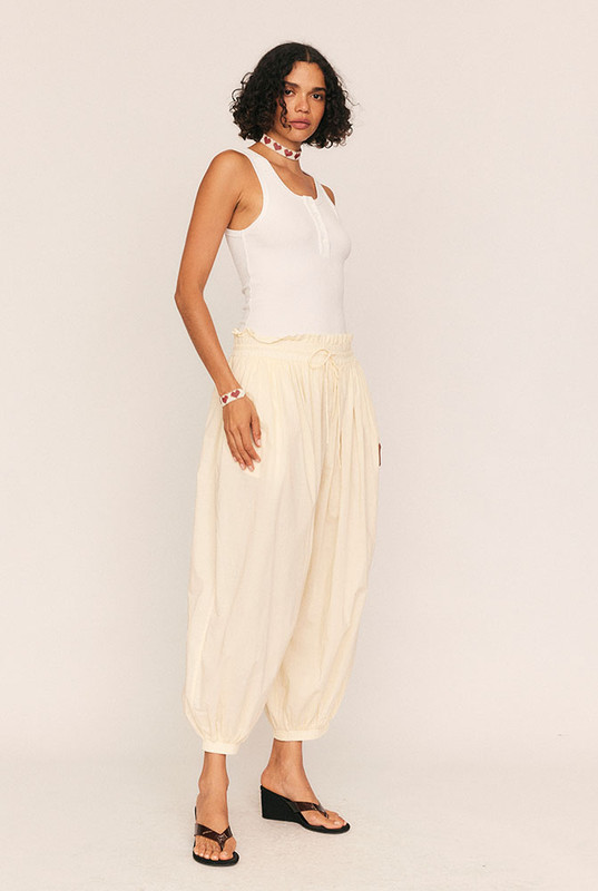 Breezy, billowing, and beautifully undone. The Genie Pant in soft Buttermilk is your invitation to float through the day with ease. Crafted from lightweight cotton voile, this ankle-grazing silhouette features a smocked elastic waist and cuffs for all-day comfort, while a waist drawcord and side seam pockets add subtle functionality.