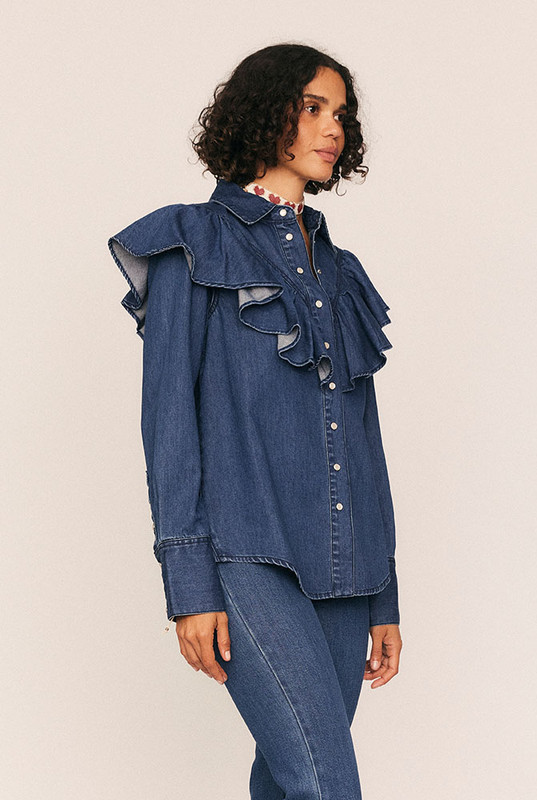 A timeless staple with a romantic edge, the Ruffle Denim Shirt redefines denim shirting with soft structure and thoughtful detail. Crafted from premium mid-weight cotton denim, it features a circular frill tracing the front and back yoke—bringing movement and femininity to a classic silhouette.