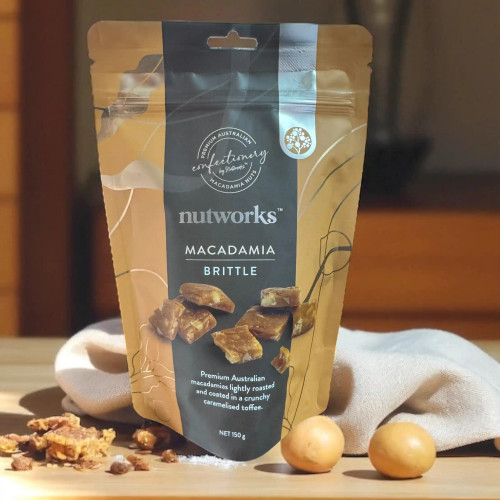 Nutworks Macadamia Brittle 150g – Premium Australian brittle with roasted macadamias in caramel toffee, standing on a wooden bench with scattered brittle pieces