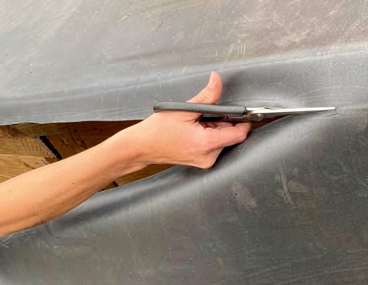 A hand lifting the edge of a black EPDM rubber membrane on a roof