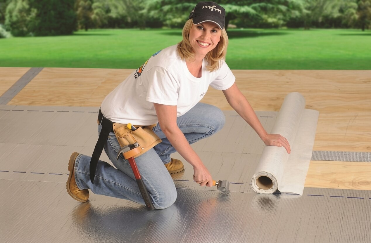 Person on a roof rolling out a silver Peel and Seal membrane