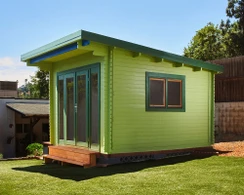 Modern Astoria garden shed painted in a bright sage green finish, featuring dark green trim and large glass doors to create a stylish backyard home office.