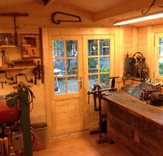 Workshop inside a shed — a workbench with a vise, hand tools on the wall and glazed double doors looking onto a garden
