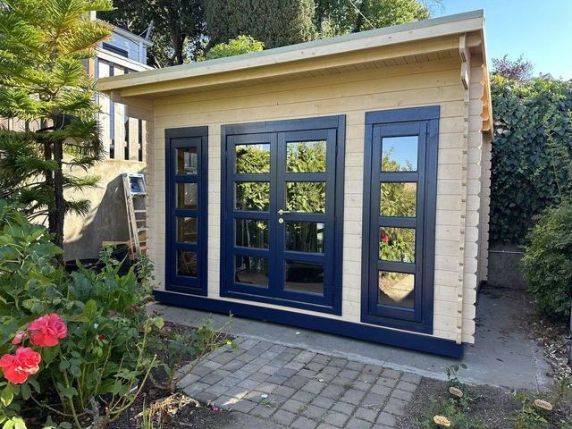 California modern shed painted cream with navy trim, on a brick patio with red geraniums