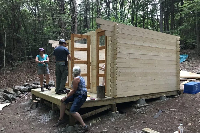 Three people fitting tongue-and-groove wall boards on a customer's shed, standing on the level timber platform that sits on concrete blocks