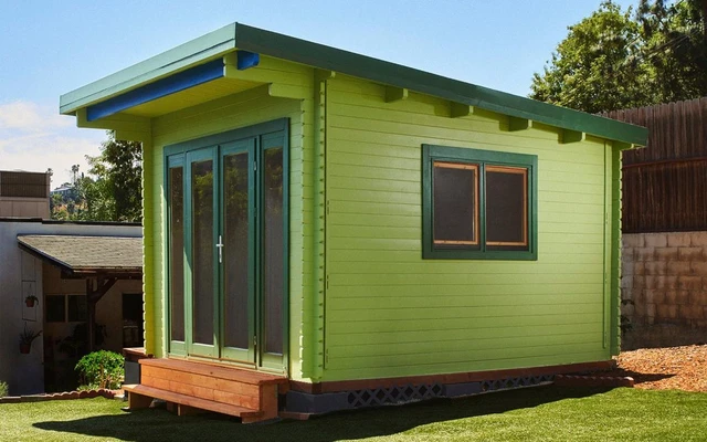 Paint preview tool: the California shed rendered in dark forest green with cream trim and a rolled-asphalt roof, beside the finish picker showing stain, neutral and color families