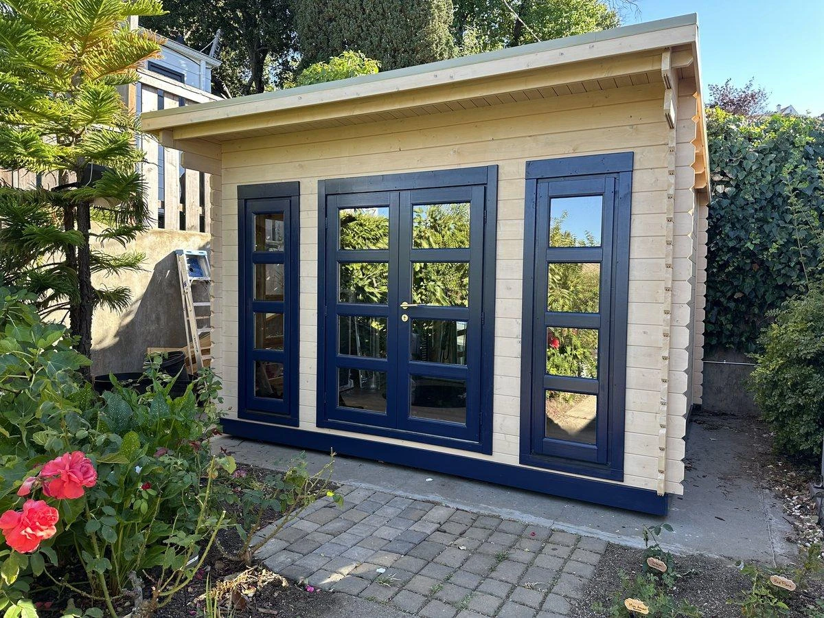 California modern shed painted cream with navy trim, on a brick patio with red geraniums