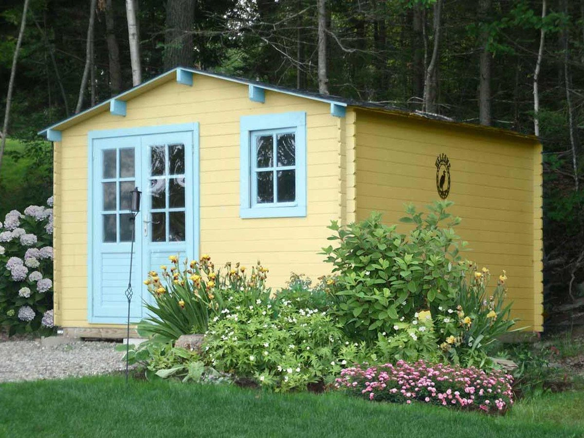 Optima classic shed painted buttercream yellow with sky-blue trim, flower bed along the front