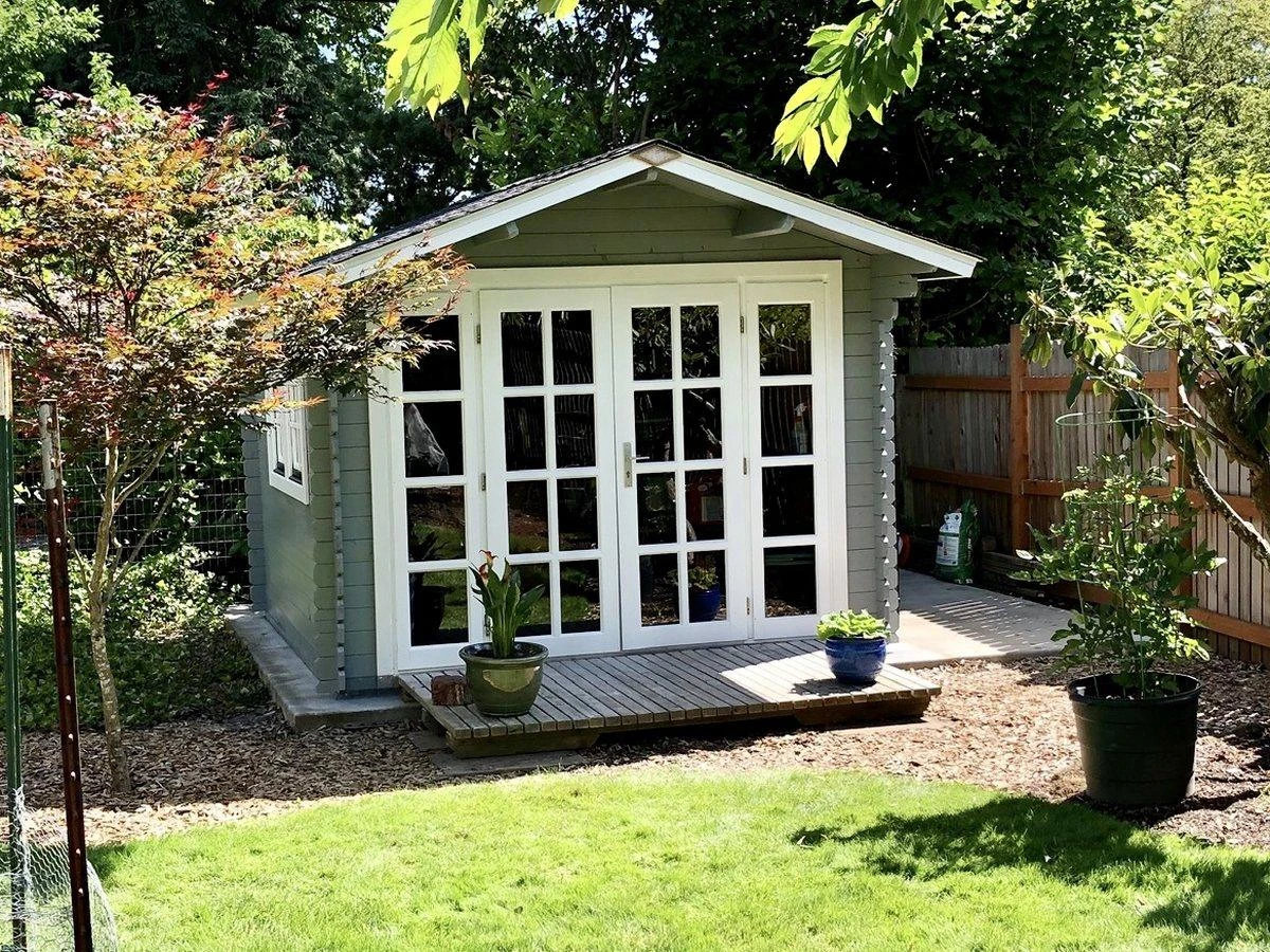 Sage-green cottage shed with white French doors and a small deck, Japanese maple alongside