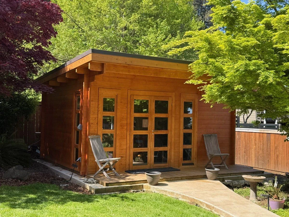 Natural cedar shed with French doors and a deck, framed by spring trees