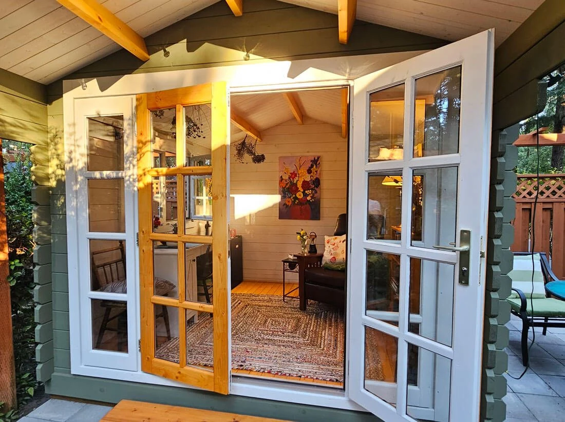 Golden-hour light through open French doors into a reading room she shed