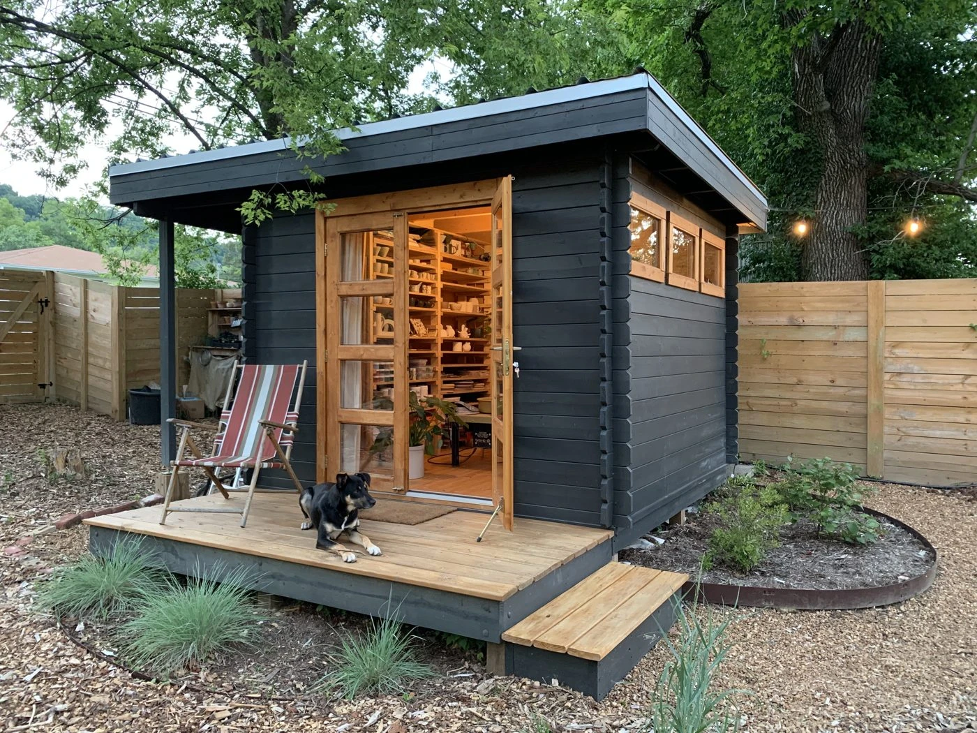 Dark-painted Solana pottery studio shed with a glowing interior and a dog on the deck