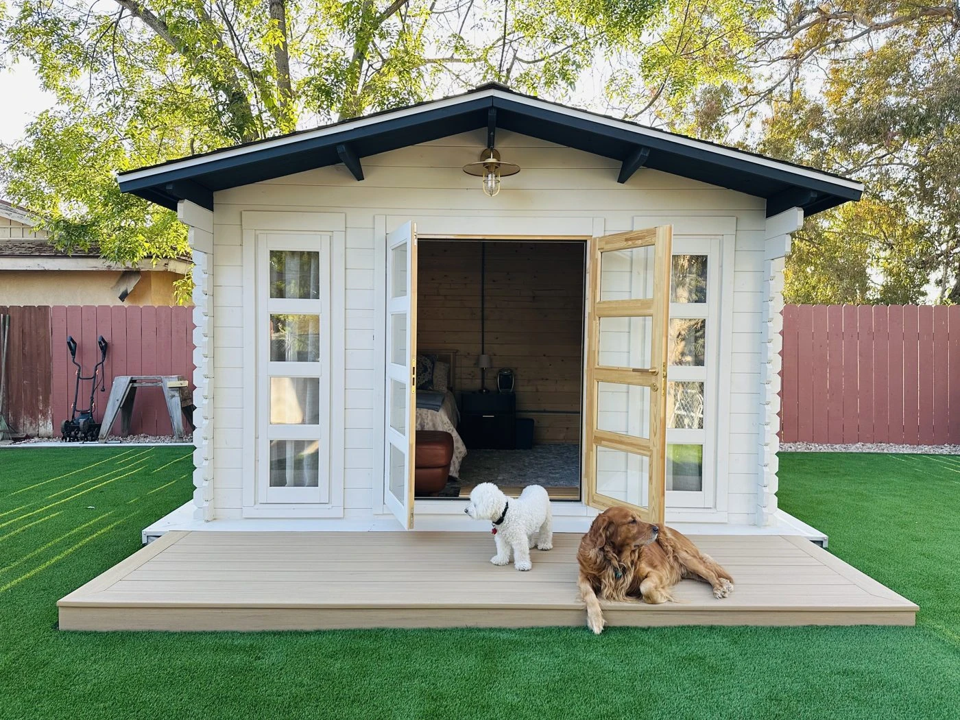 White farmhouse-style shed with open double doors and two dogs on the lawn
