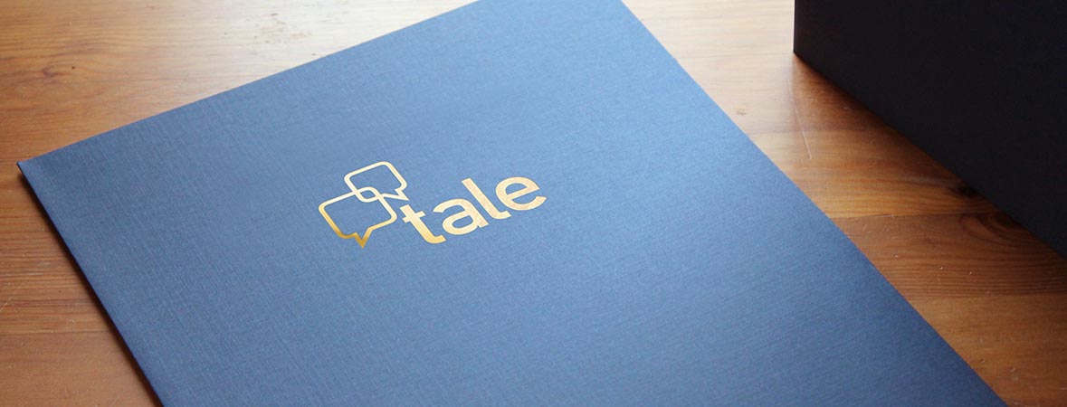 A blue pocket folder lies on a desk and has a gold foil logo imprint on the front cover.