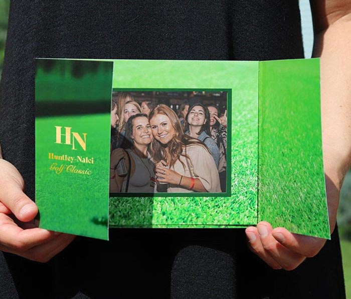 A woman in a black dress holds a golf gatefold photo folder designed with a golf course look.